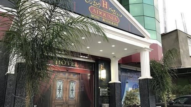 A hotel entrance with a dark facade, a prominent 'HOTEL' sign above the door, and a small tree to the left. - Hôtel Adounia (Ouled Moussa)