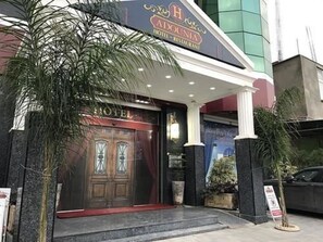 A hotel entrance with a dark facade, a prominent 'HOTEL' sign above the door, and a small tree to the left. - Hôtel Adounia (Ouled Moussa)