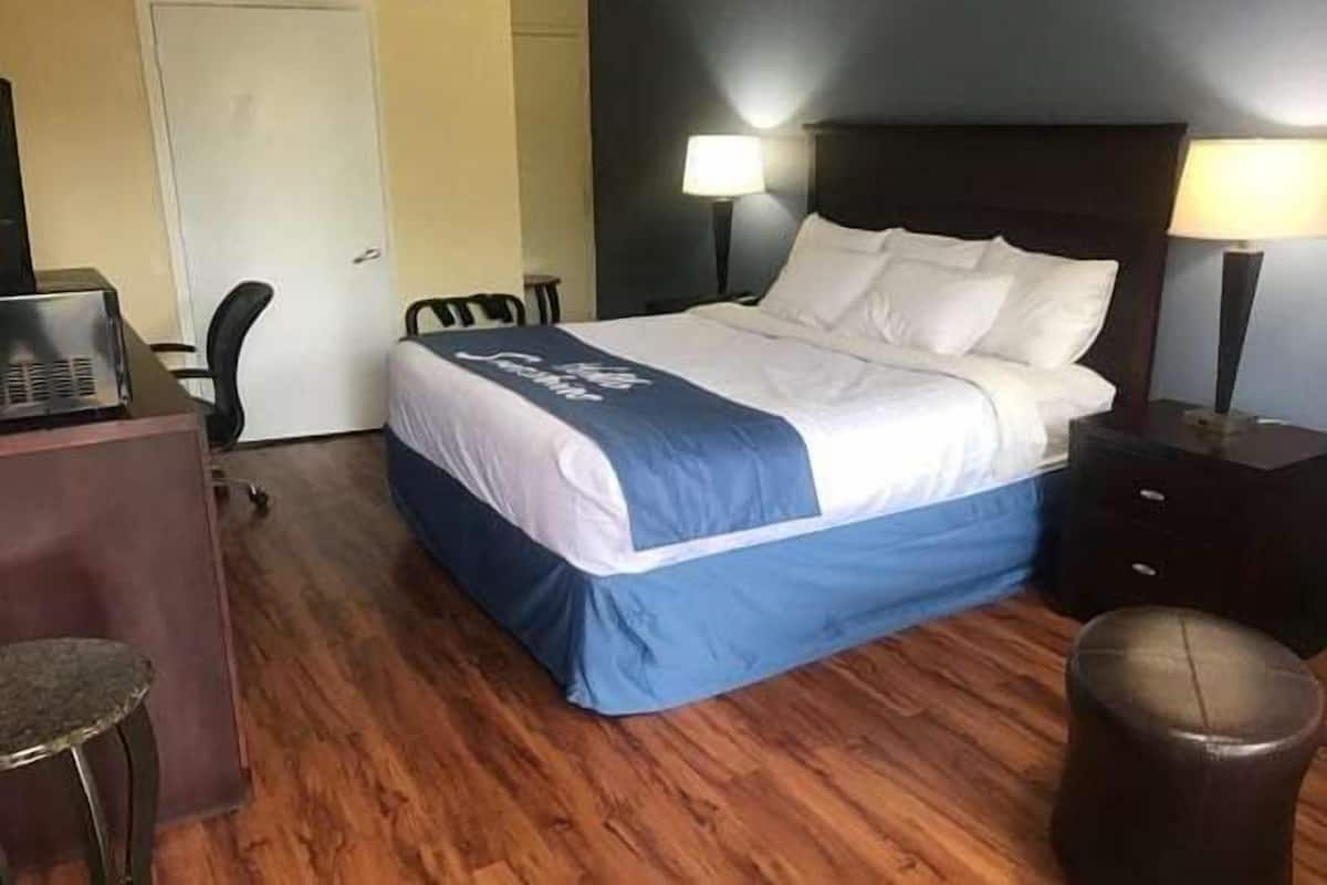 A hotel room with a bed, a desk, a chair, and a lamp.