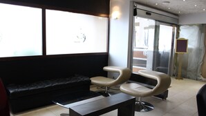 Une salle d’attente avec un canapé noir, deux fauteuils beige et une petite table.