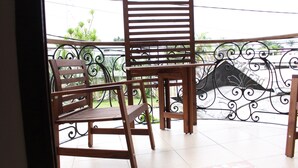 A balcony with two wooden chairs and a table, featuring a decorative metal railing and a view of greenery.