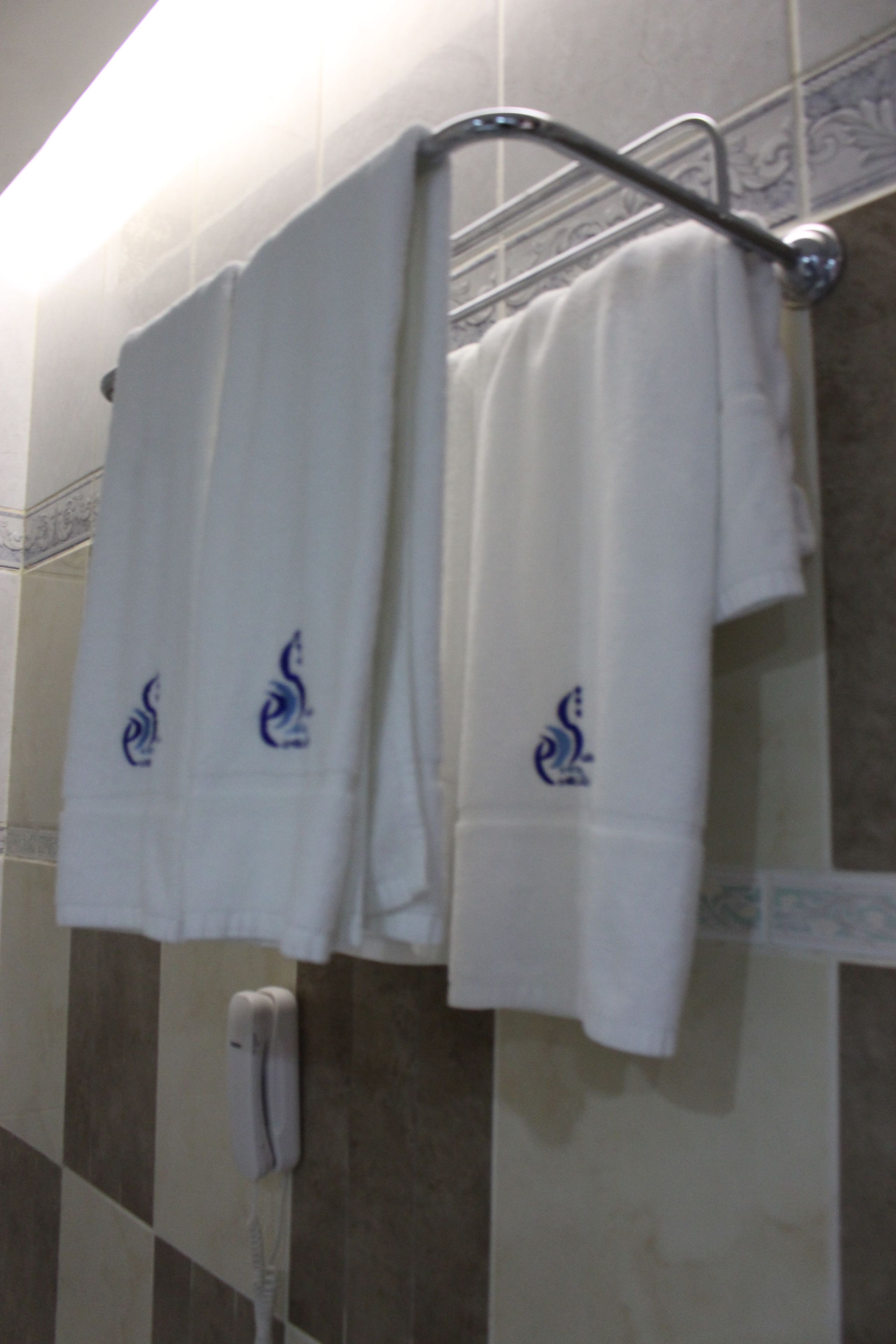 A bathroom with two white towels hanging on a metal rack, a white telephone, and patterned tiles on the wall.
