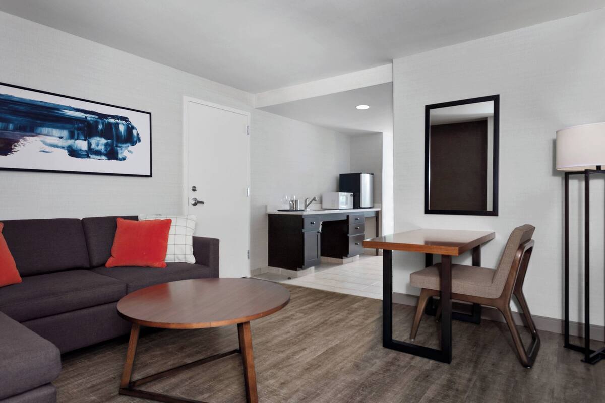 A modern living room with a dark sofa, a round wooden coffee table, and a dining area with a small table and chair.