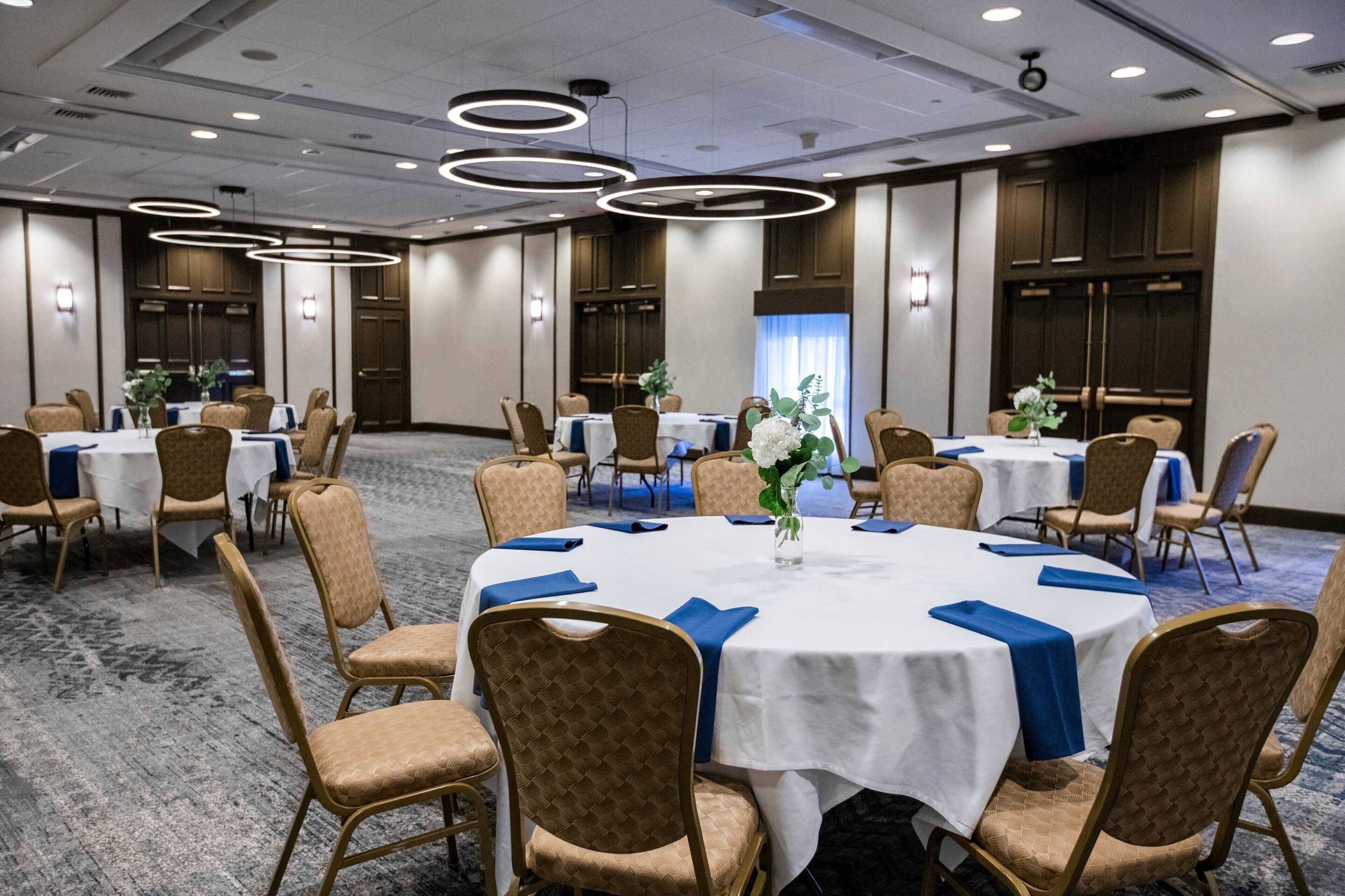 Un salón de conferencias con mesas redondas, sillas color beige y manteles azules.