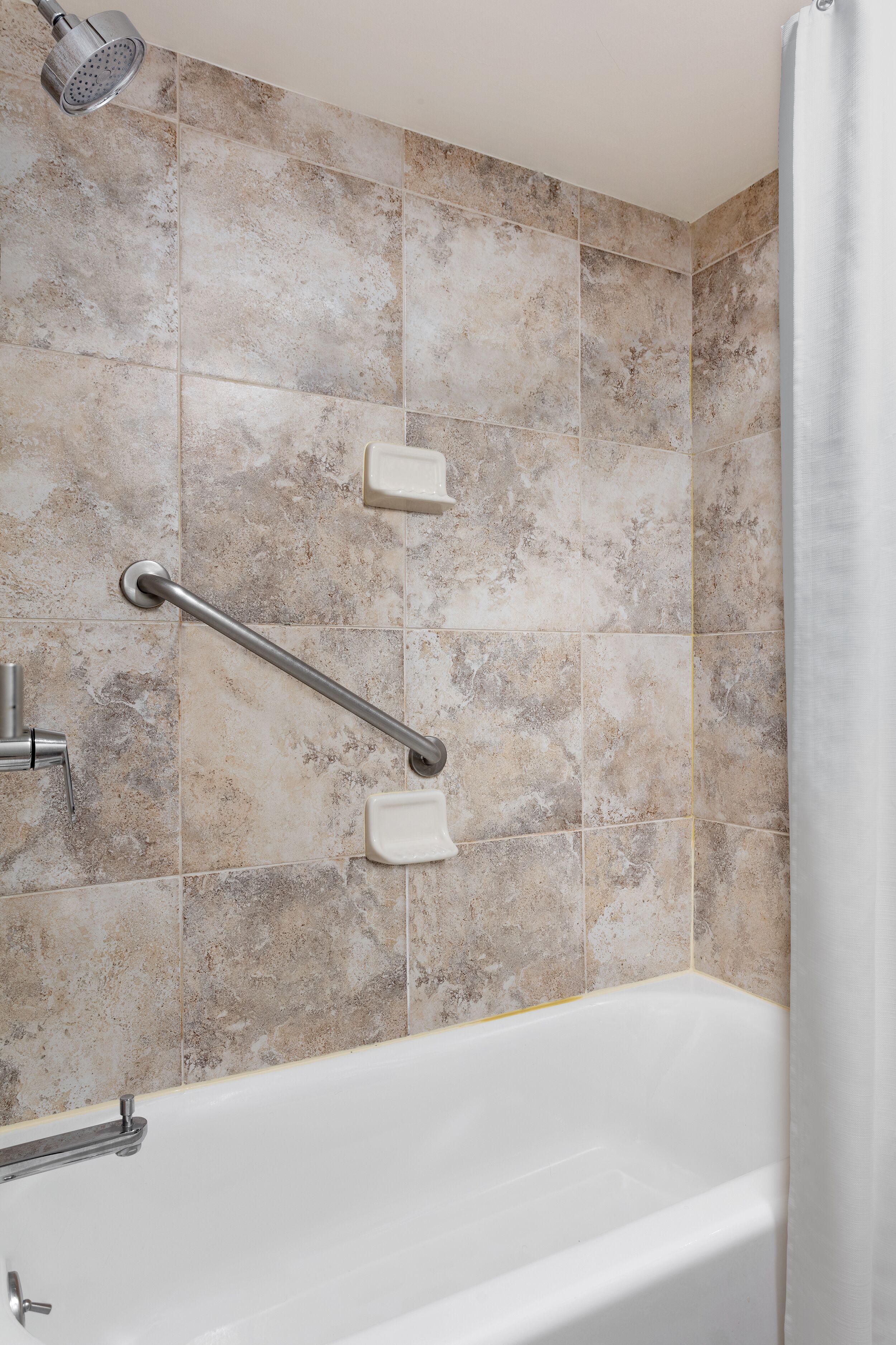 A bathroom with a bathtub, grab bars, and a showerhead.