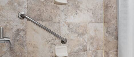 A bathroom with a bathtub, grab bars, and a showerhead.