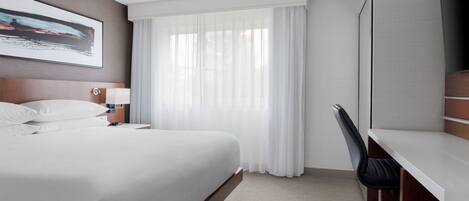 A hotel room with a bed, a desk, a chair, a TV, and a window with curtains.