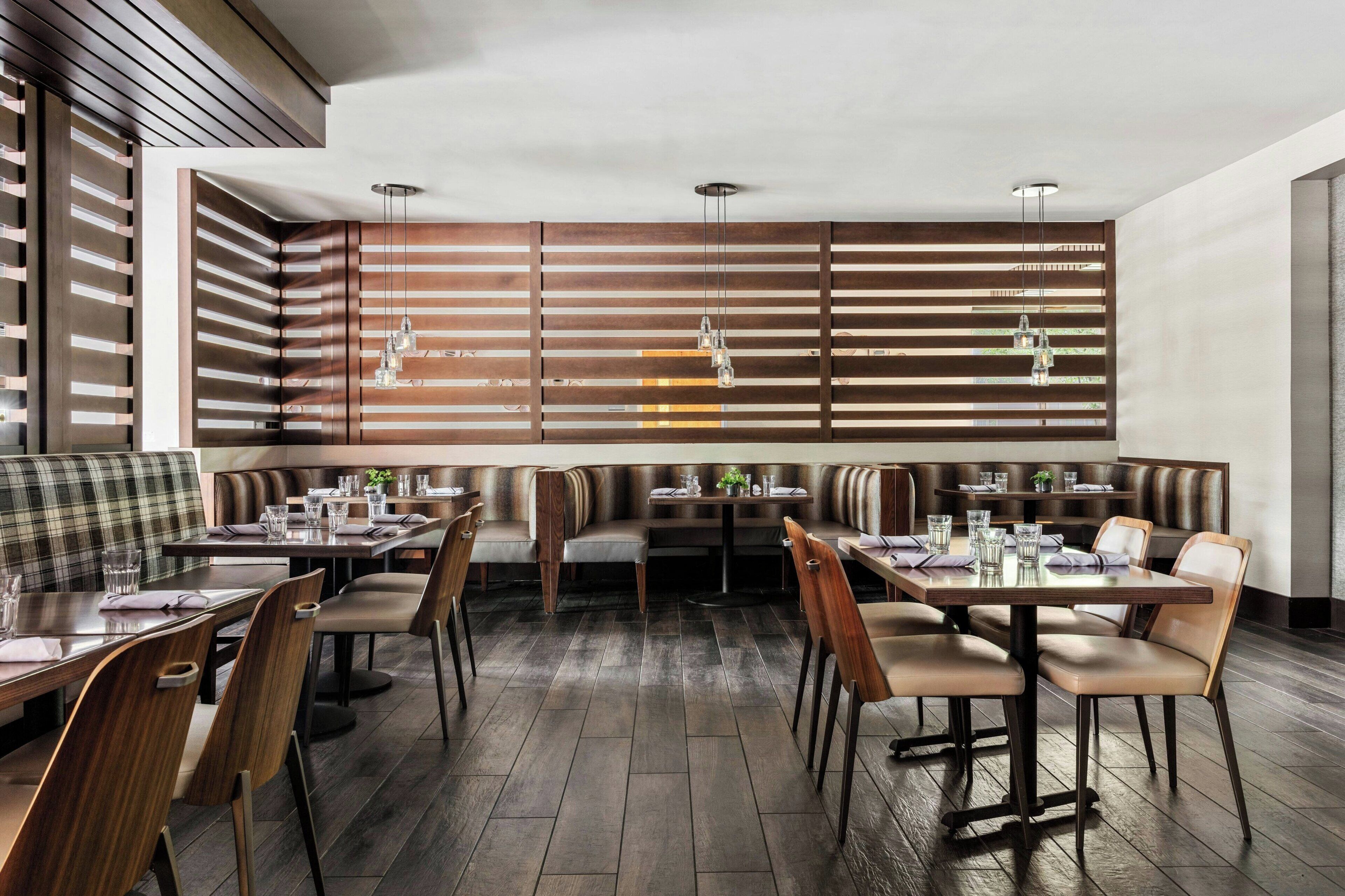 A modern restaurant with wooden slatted walls, multiple seating areas including booths and tables, and pendant lighting.