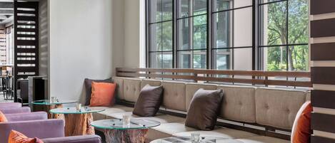 A modern lounge area with a sofa, cushioned chairs, and round glass tables.
