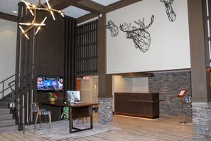 Um hall de entrada com balcão de recepção, computador, televisão exibindo esportes e escada.