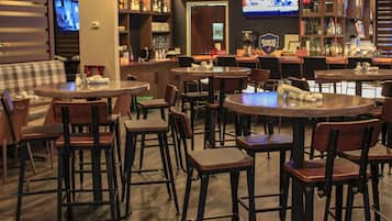 Een barruimte met meerdere tafels en stoelen, een televisiescherm en een bar gevuld met diverse flessen.