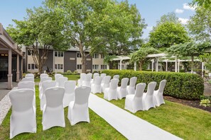 A row of white chairs with a white aisle in a courtyard with buildings in the background. - Delta Hotels by Marriott Burlington (South Burlington)