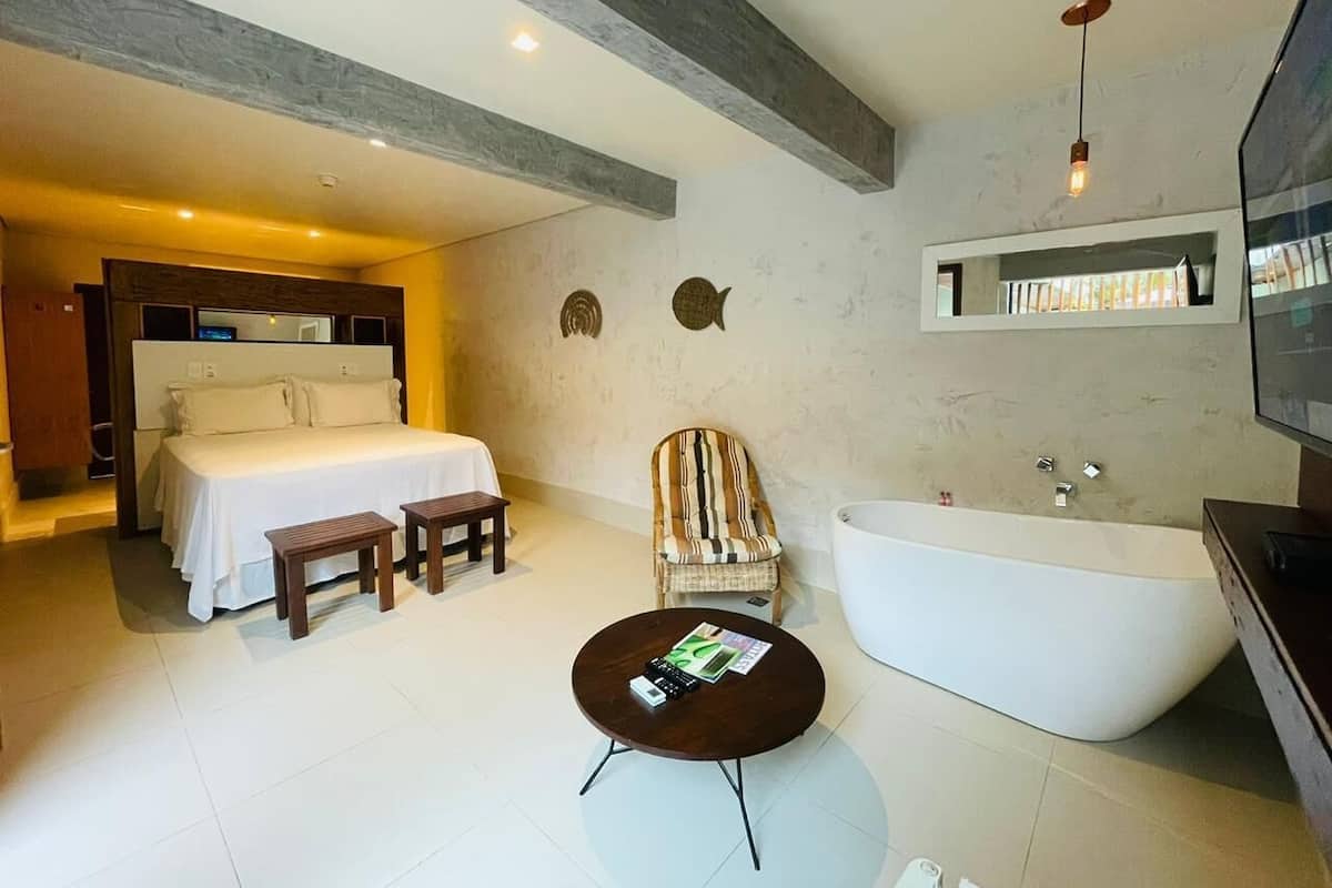 Une chambre d’hôtel moderne dotée d’un grand lit, d’un coin salon avec une table ronde, d’une baignoire et d’un téléviseur.