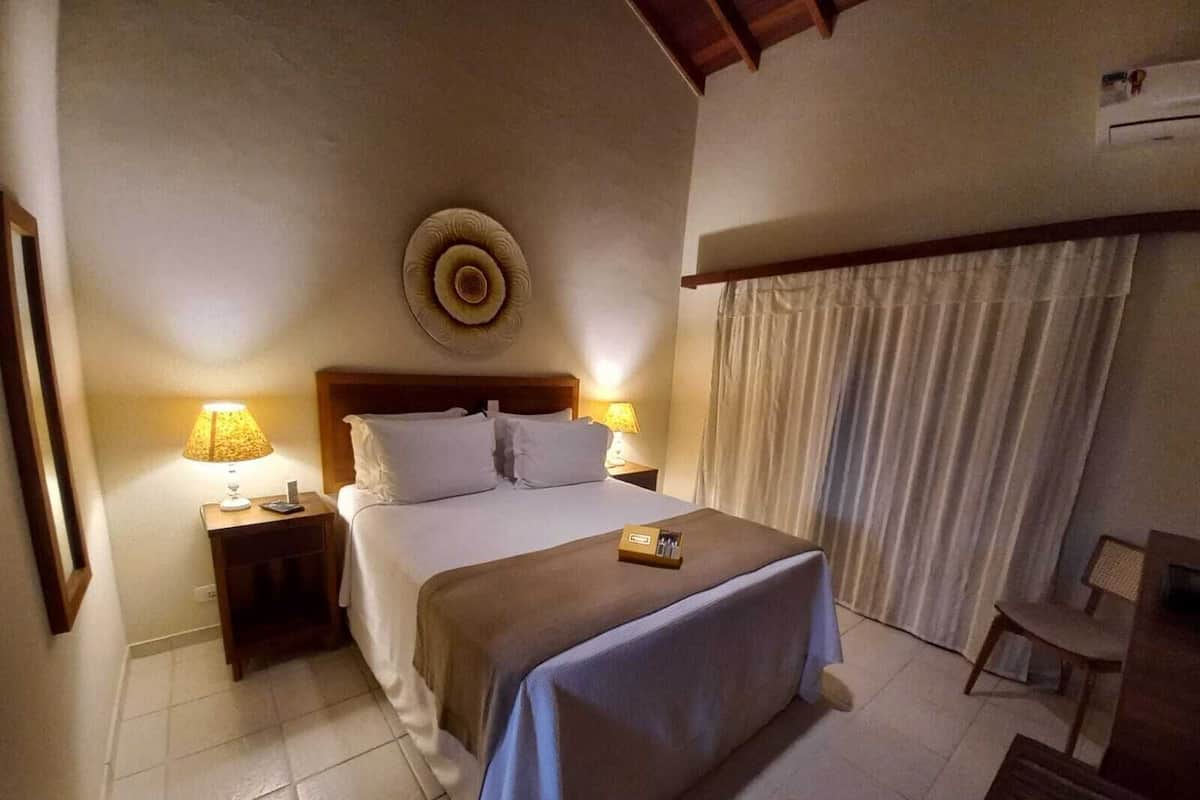 Une chambre d’hôtel comprenant un lit, deux tables de chevet, une lampe, un élément de décoration murale et un rideau.