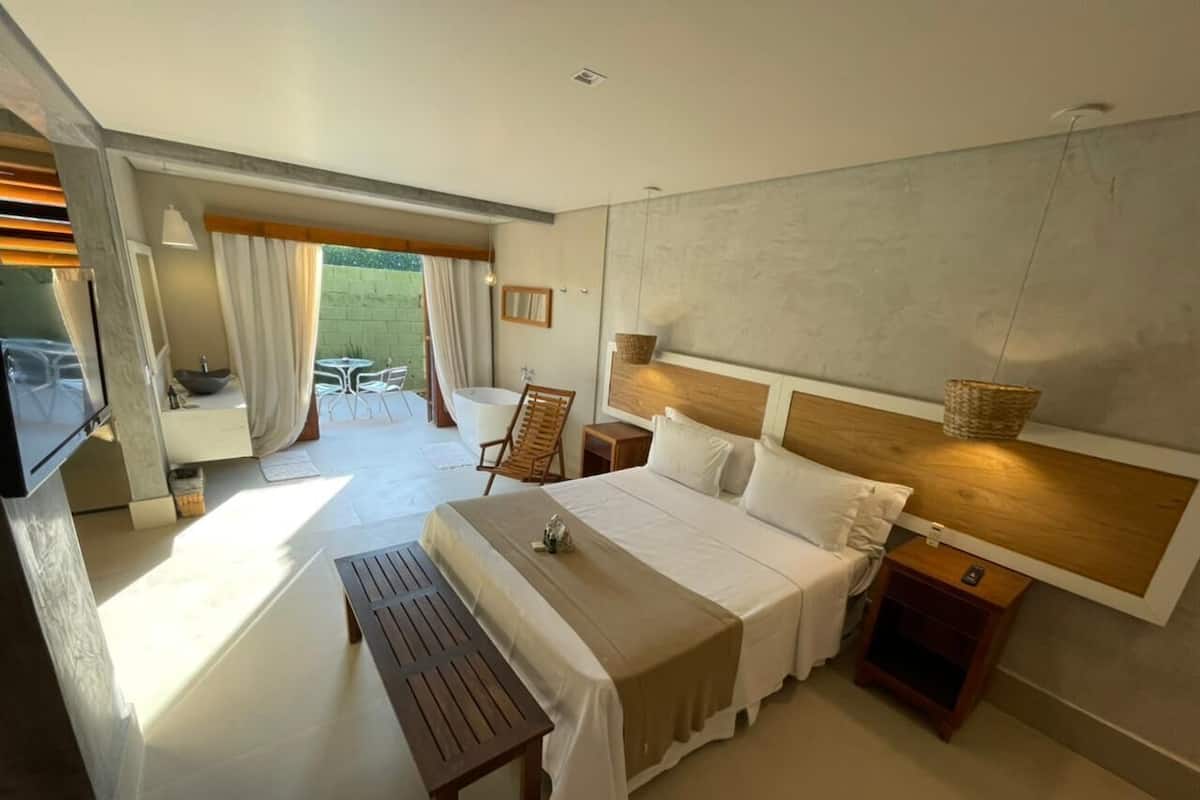 Une chambre d’hôtel moderne avec un grand lit, un banc en bois, une petite table et une vue sur l’extérieur.