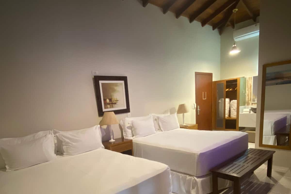 Une chambre d’hôtel avec deux lits, un banc en bois, un tableau encadré au mur et une armoire.