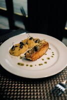 Een bord met een stuk zalm, twee kleine aardappelen en garnering op een wit bord.