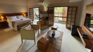 A hotel room with a bed, a sofa, a small table, a TV, and a balcony with a view. - Hiu Hotel (São Sebastião)