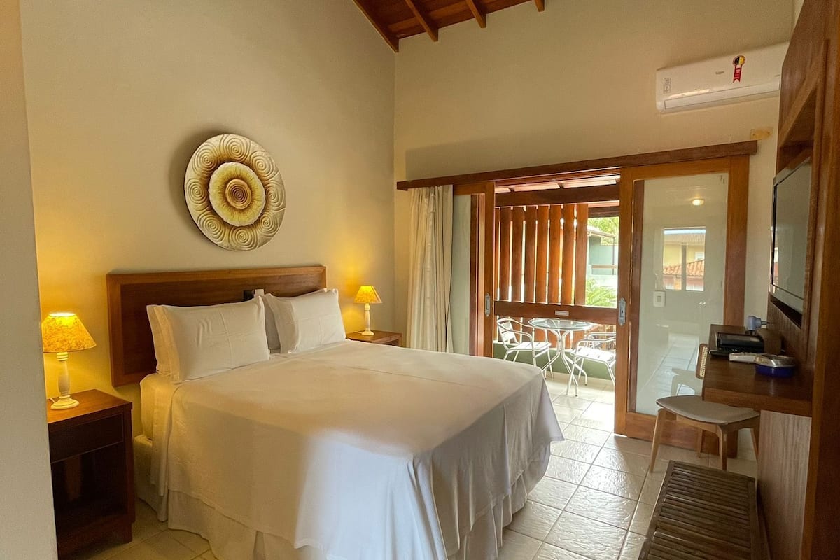 Une chambre d’hôtel avec un grand lit, un plafond en bois, une assiette décorative accrochée au mur, une télévision et une petite table avec une lampe.