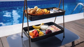 A breakfast tray with fruits, pastries, and beverages by a poolside. - Hiu Hotel (São Sebastião)