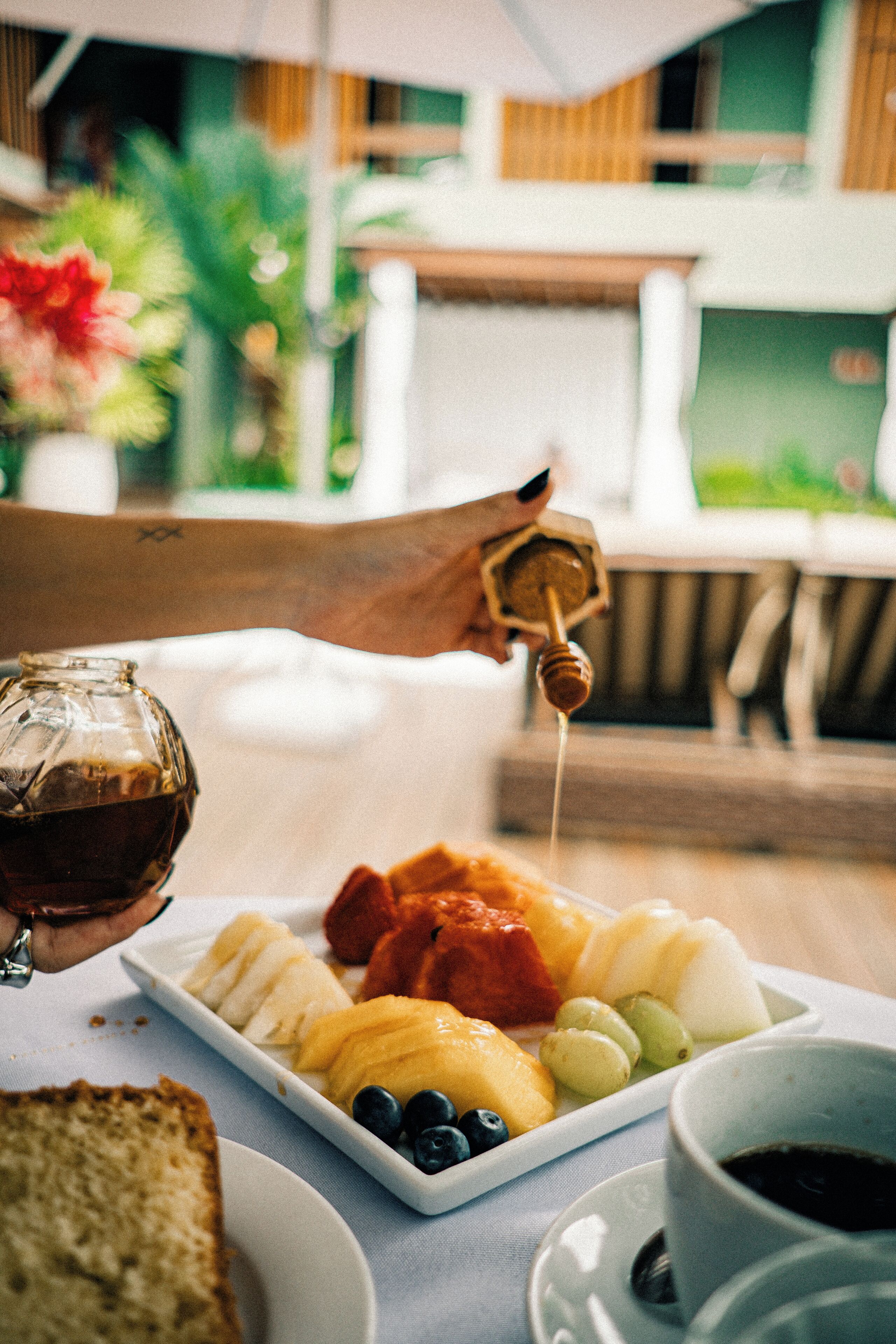 A breakfast setting with a plate of fruits, a glass of coffee, and a honey dipper.