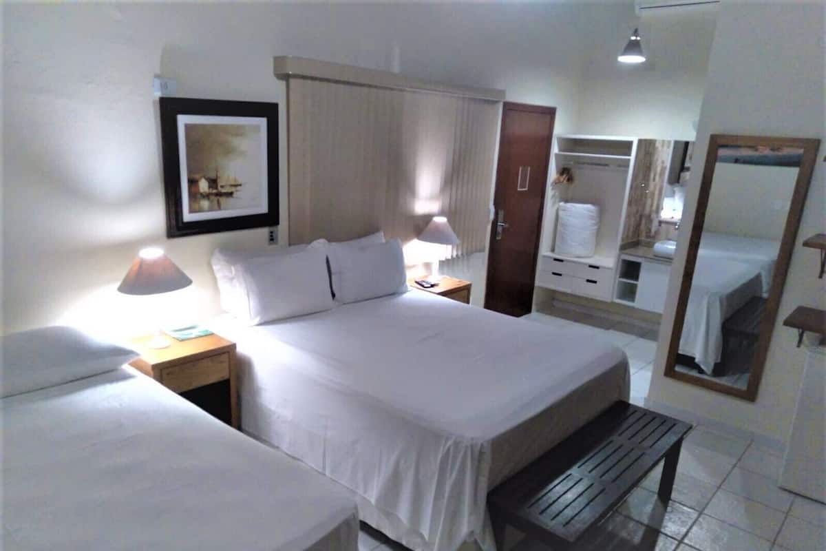 Une chambre d’hôtel comprenant un lit, des tables de chevet, un banc, une armoire, un miroir et un tableau encadré au mur.