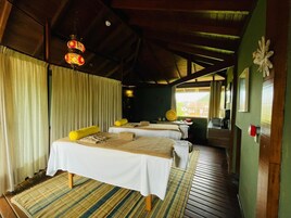 Una habitación con dos camas, techo de madera, una ventana y una pequeña mesa con lámpara.