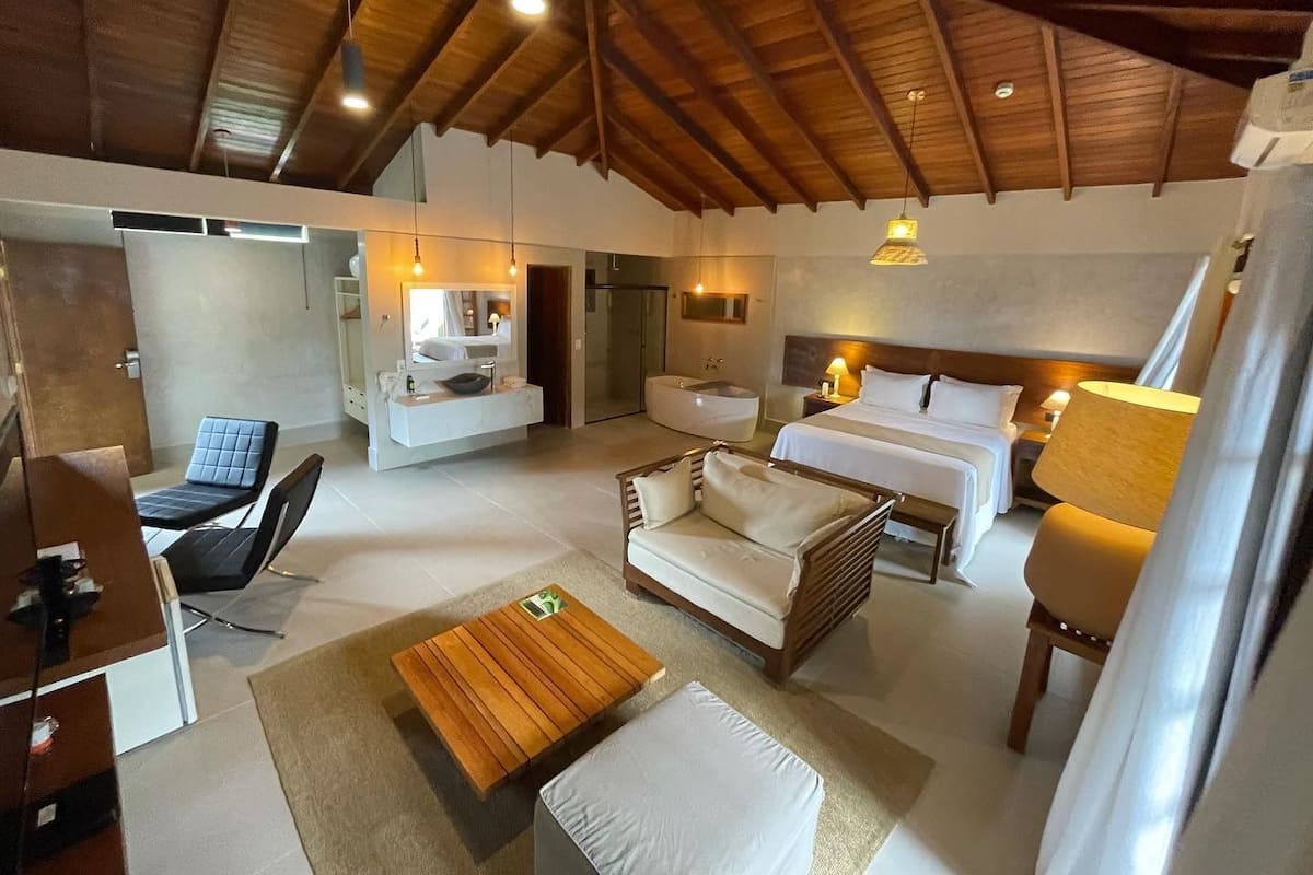 Une chambre d’hôtel moderne dotée d’un grand lit, d’un coin salon avec un canapé et des fauteuils, d’une table basse en bois et d’une salle de bain avec baignoire.