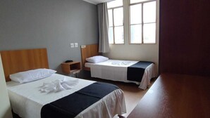 A hotel room with two beds, a wooden headboard, a small bedside table, and a window with curtains. - Hotel La Rocca, Goiânia  (Goiania)