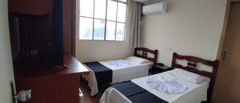 Een hotelkamer met twee enkele bedden, een houten bureau, een stoel en een raam met gordijnen.