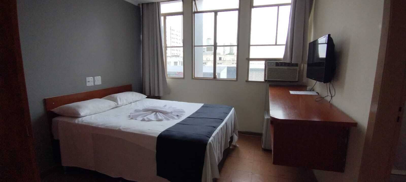 A hotel room with a bed, a desk, a television, and a window with curtains.