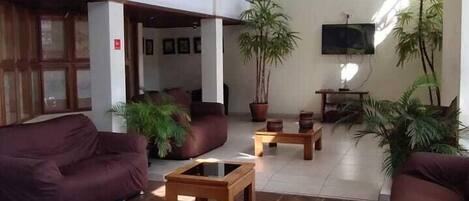 A spacious lobby with a high ceiling, large windows, and a modern design. There are several seating areas with sofas and a coffee table.