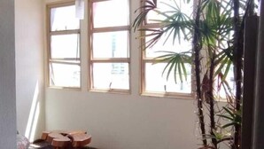 A room with wooden flooring, two windows, a potted plant, and a small wooden table. - Hotel La Rocca, Goiânia  (Goiania)