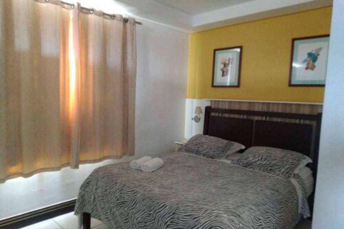 A bedroom with a bed, curtains, a headboard, and two framed pictures on the wall.