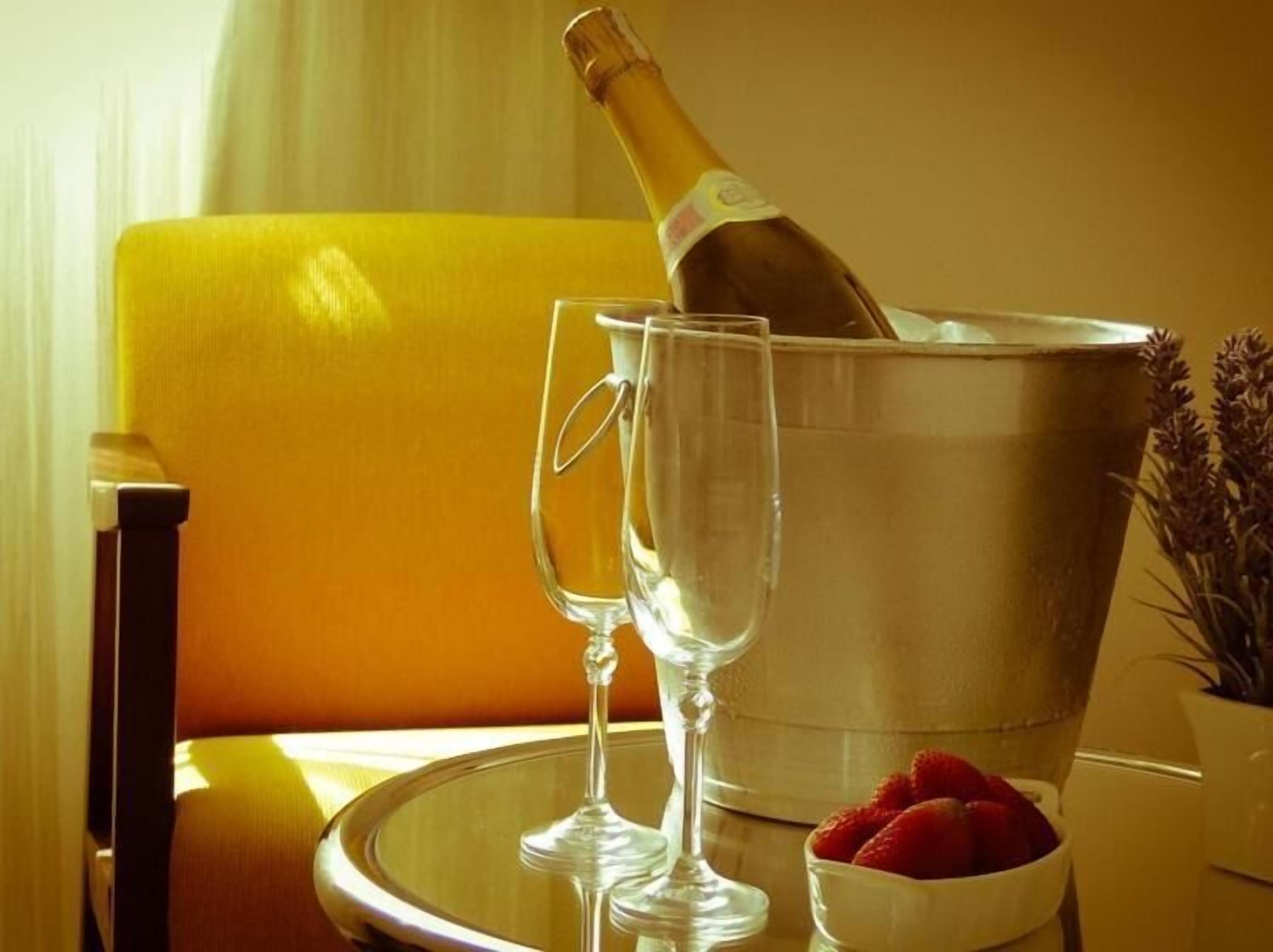 A champagne bottle in a metal bucket, two empty wine glasses, a bowl of strawberries, and a yellow chair.