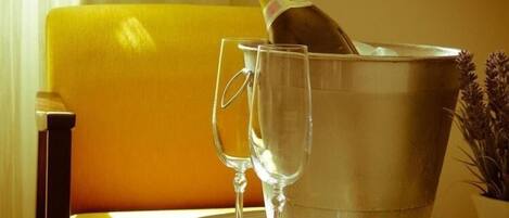 A champagne bottle in a metal bucket, two empty wine glasses, a bowl of strawberries, and a yellow chair.