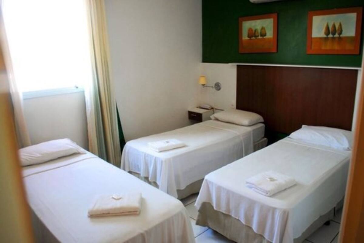 A hotel room with two single beds, a nightstand, a lamp, and two paintings on the wall.