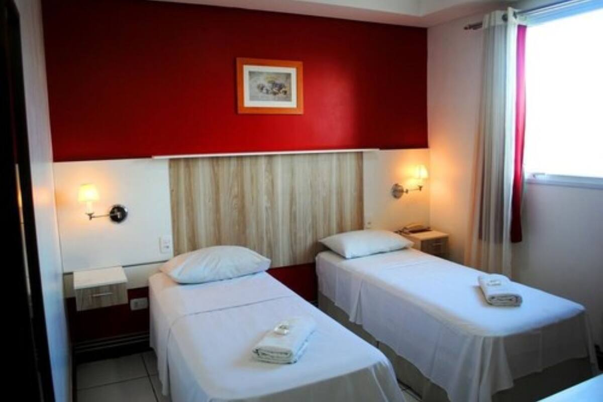 A hotel room with two single beds, a red accent wall, and a framed picture above the beds.