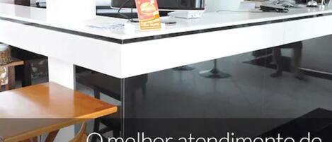 A reception desk with a Samsung monitor, a flower vase, and a snack box.
