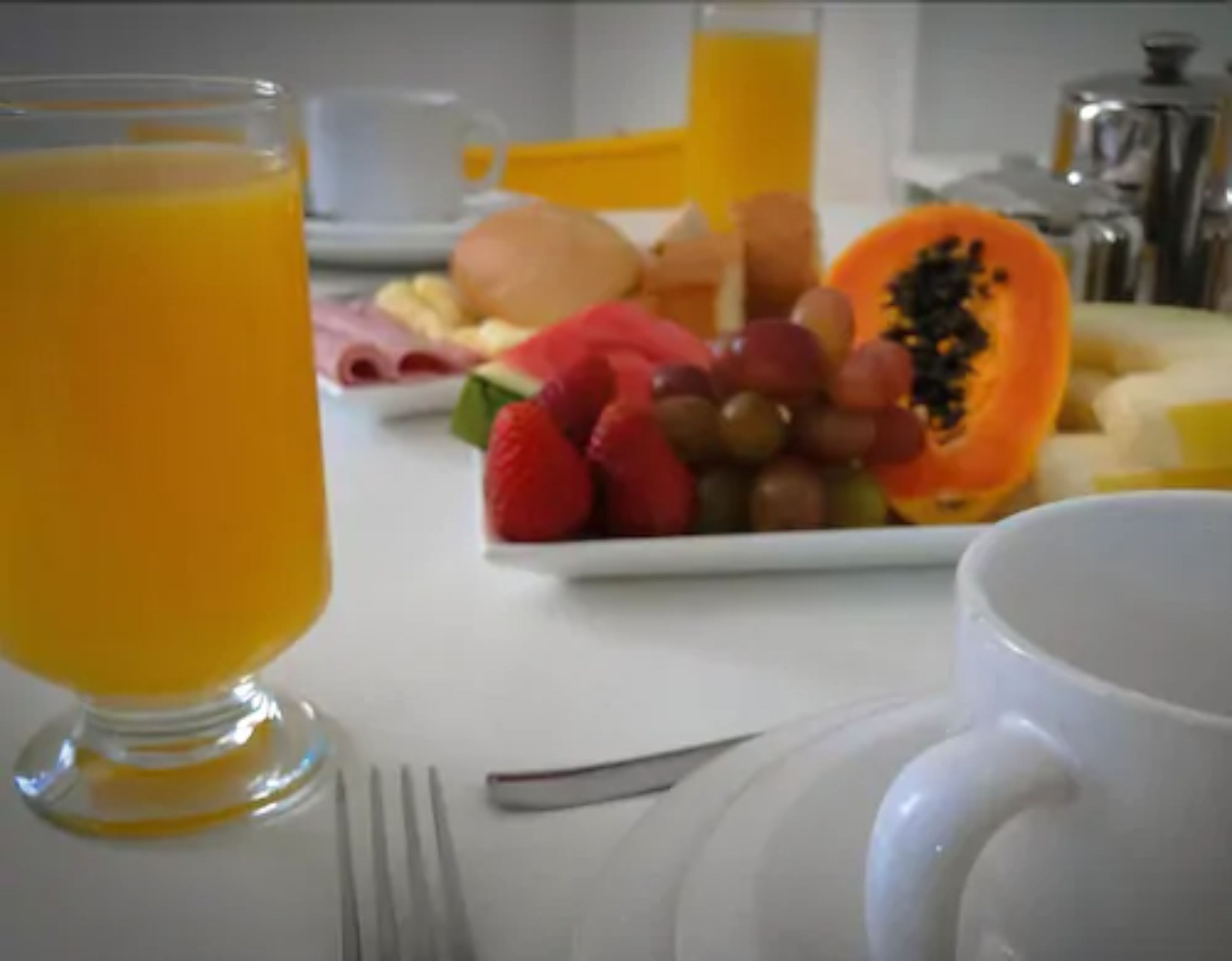Een ontbijttafel met een glas jus d'orange, een schaal fruit en een witte mok.