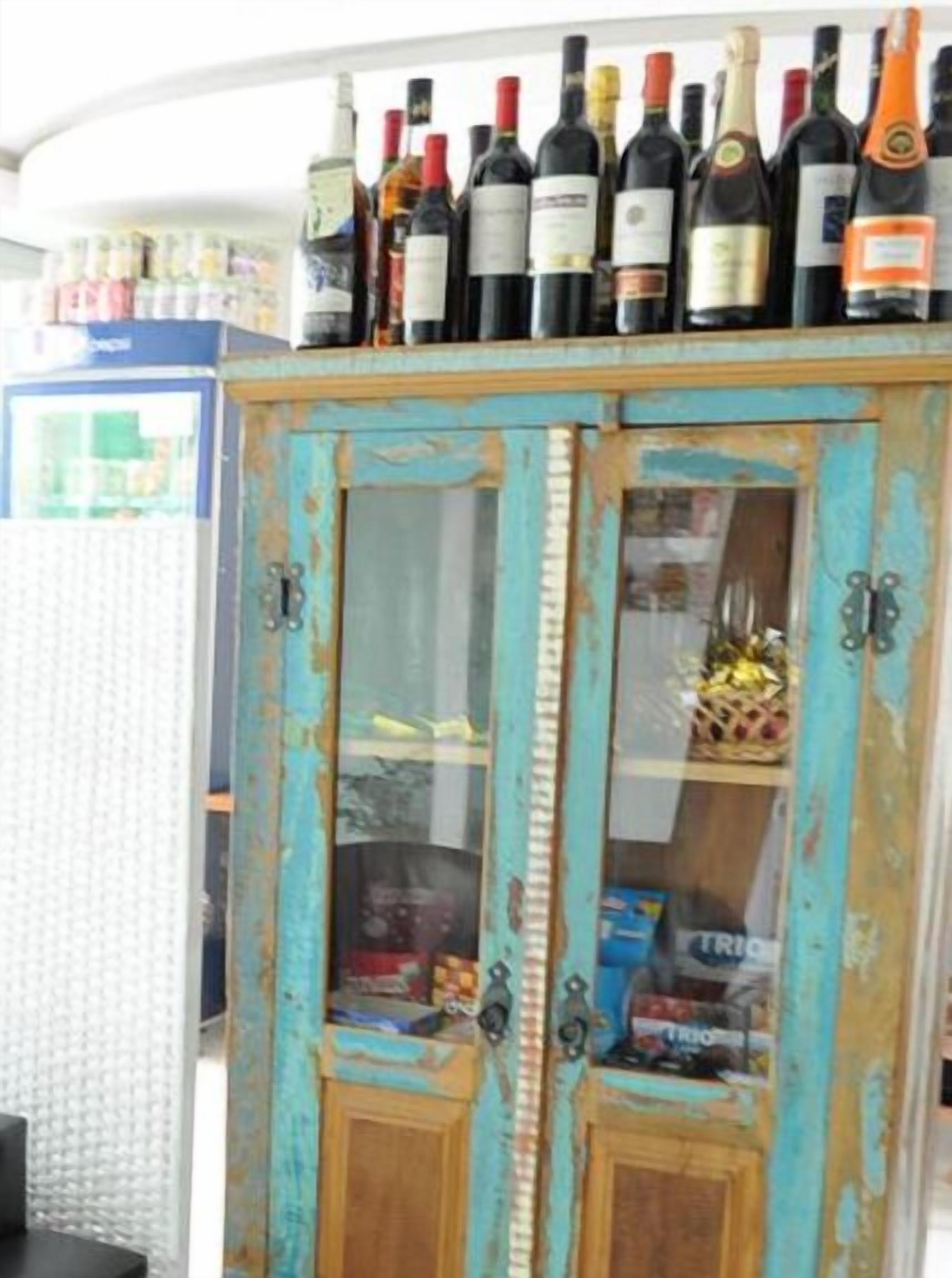 Un mueble de madera rústico y desgastado con puertas de cristal, que contiene varias botellas y objetos.