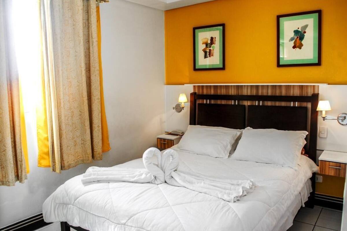 A hotel room with a bed, two nightstands, a headboard, and two framed pictures on the wall.