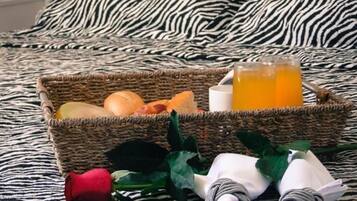 Una cama con colcha de estampado de cebra, una cesta tejida con frutas y un vaso de jugo de naranja, y una rosa roja sobre la cama.