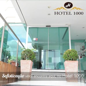 The entrance of Hotel 1000 with a modern glass facade, potted plants, and a sign indicating payment options. - Hotel 1000 (Piracicaba)