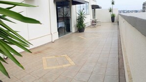 En flisebelagt udendørs terrasse med glasdør, plantekasser og et lille bord med stole.