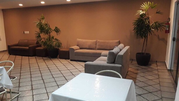 Et værelse med flisegulv, beige sofa, grå sofa, et hvidt bord og to krukker med planter.