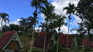 A row of A-frame cabins with stone walls and red roofs, surrounded by lush greenery and palm trees. - Phunaya Resort (Khao Kho)