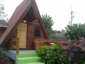 A wooden cabin with a steeply pitched roof, a front door, and a small porch. - Phunaya Resort (Khao Kho)