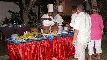 Disposição de buffet com toalha vermelha, diversos alimentos e pessoas servindo.