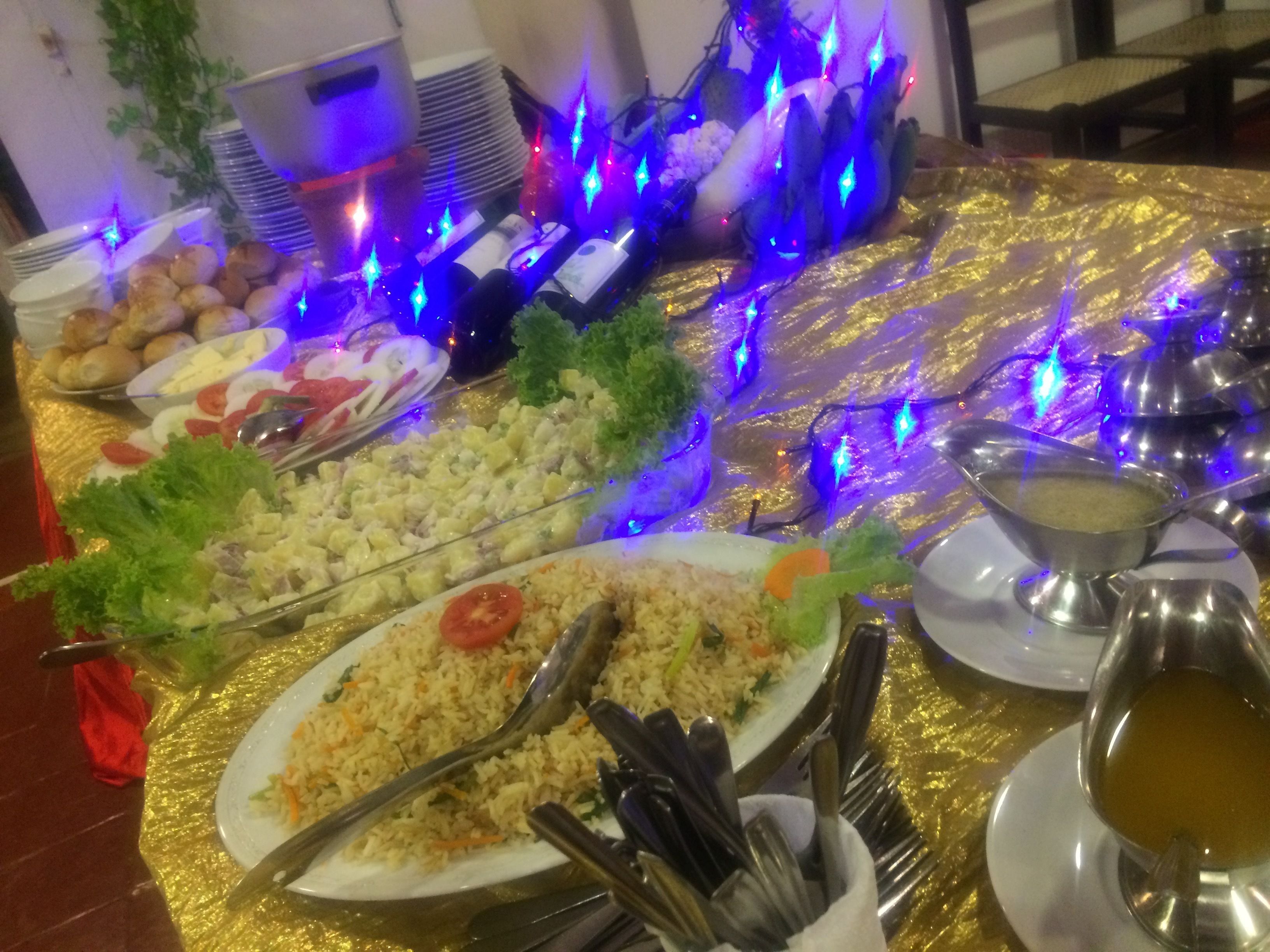 Een buffet met diverse gerechten, zoals rijst, salades en brood, op een gouden tafelkleed met blauwe decoratieve verlichting.